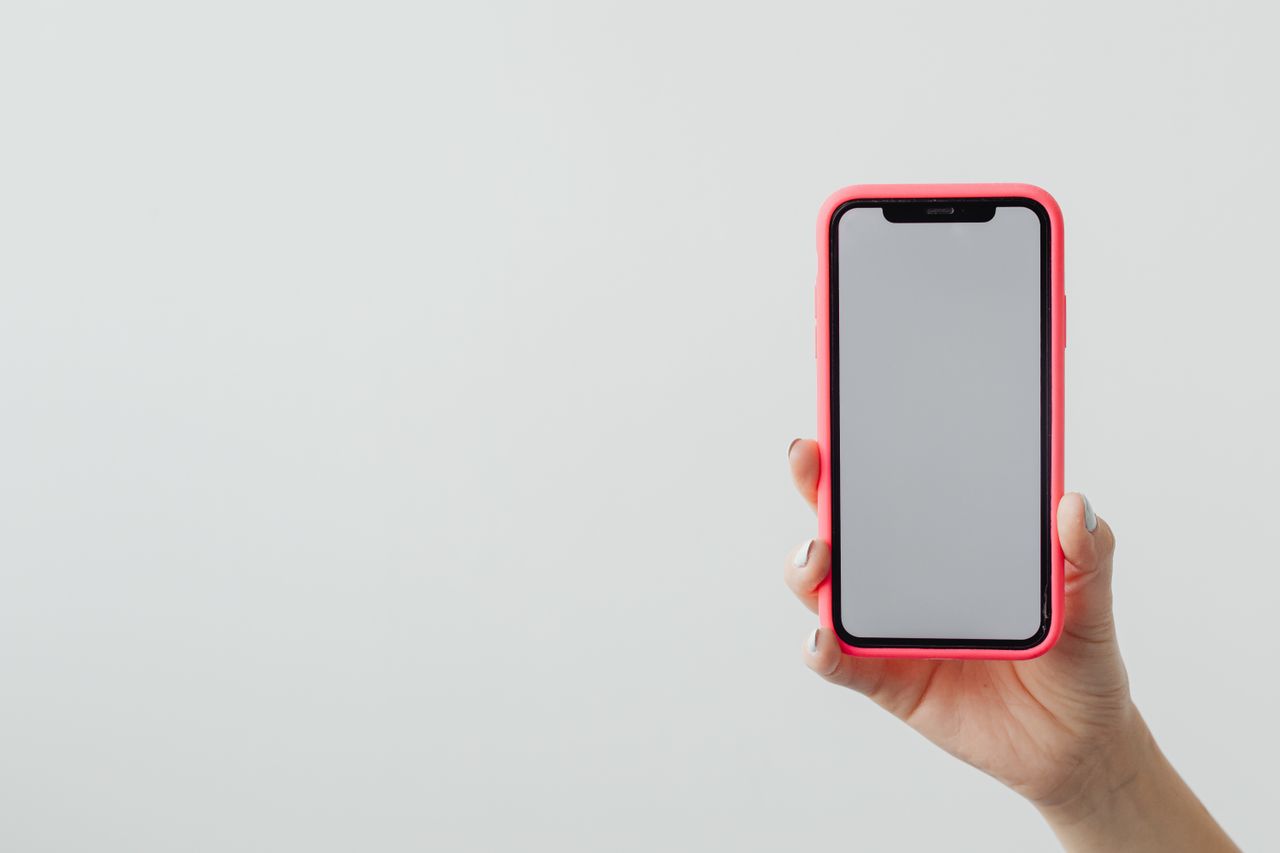 A hand holding a smartphone with a red case against a clean white background, ideal for tech concepts.